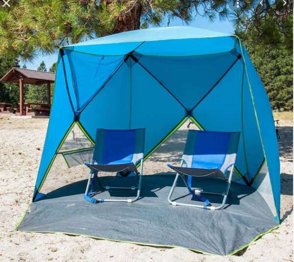 A blue tent with two chairs on the beach.
