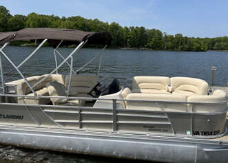 A beige pontoon boat docked at a lake.